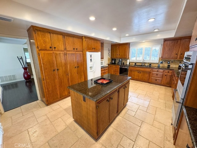 kitchen with recessed lighting, a sink, brown cabinets, a raised ceiling, and white appliances