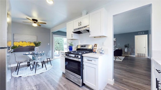 kitchen featuring white cabinets, light wood-style floors, under cabinet range hood, stainless steel gas stove, and a ceiling fan