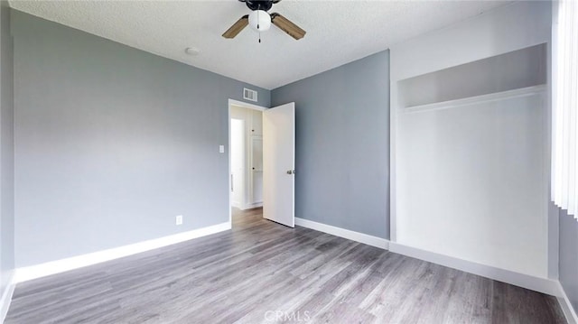 unfurnished bedroom with wood finished floors, a closet, baseboards, visible vents, and a textured ceiling