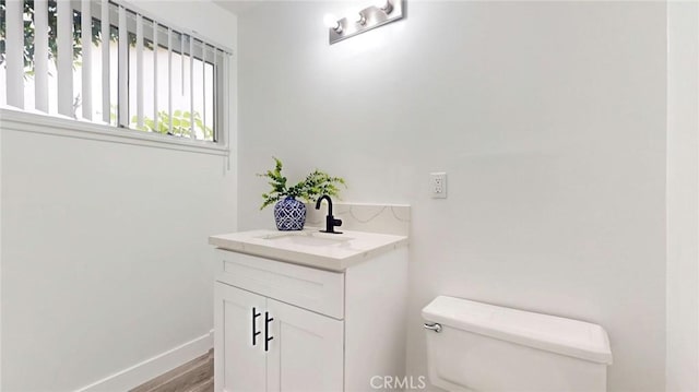 half bathroom with wood finished floors, vanity, toilet, and baseboards