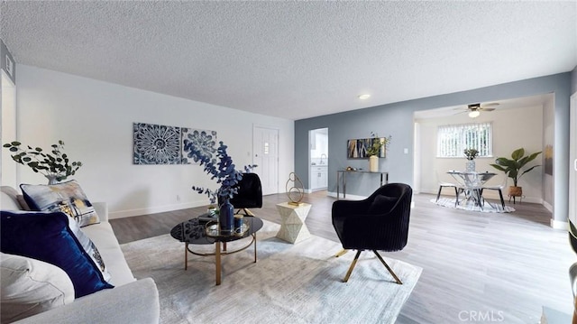 living area featuring light wood finished floors, a textured ceiling, ceiling fan, and baseboards