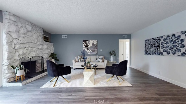 living room featuring a textured ceiling, visible vents, a stone fireplace, and wood finished floors