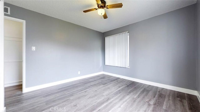 empty room with wood finished floors, ceiling fan, baseboards, visible vents, and a textured ceiling