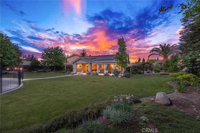 view of front of home with roof mounted solar panels, a lawn, a patio, and a fenced backyard