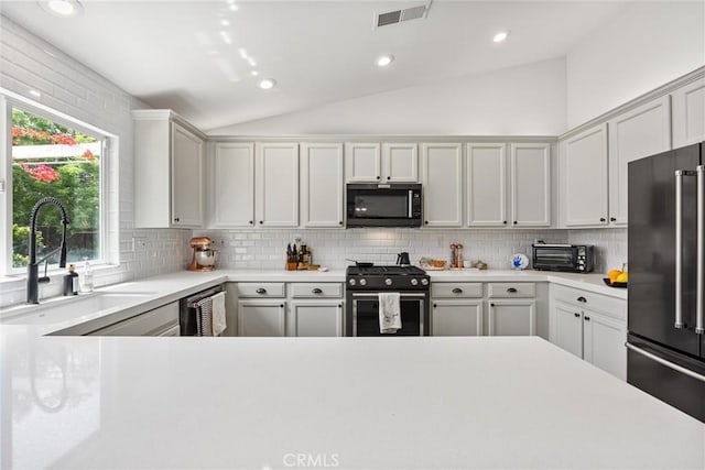 kitchen with lofted ceiling, a sink, visible vents, gas range oven, and high end fridge