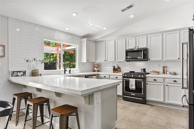 kitchen with appliances with stainless steel finishes, a sink, visible vents, a peninsula, and lofted ceiling