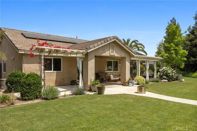 back of house featuring roof mounted solar panels, a lawn, a patio area, and stucco siding