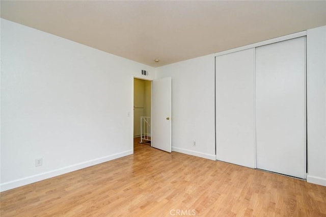 unfurnished bedroom featuring visible vents, a closet, light wood-style flooring, and baseboards
