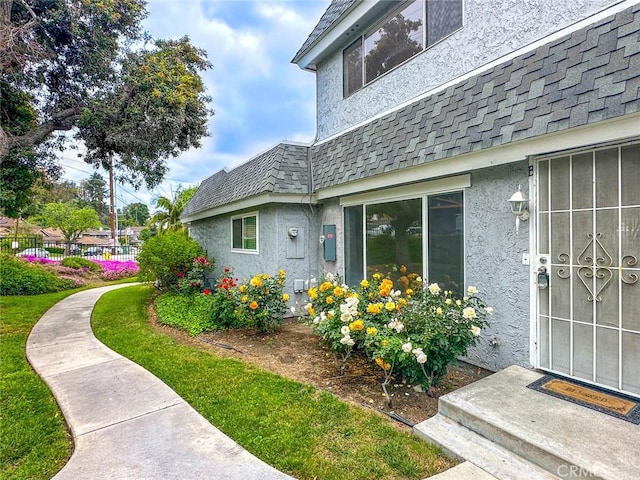 property entrance featuring fence, stucco siding, mansard roof, and roof with shingles