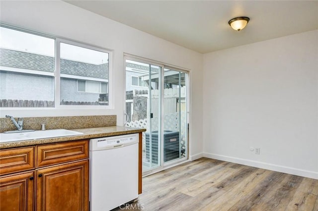 kitchen with a sink, brown cabinets, light wood-style flooring, baseboards, and dishwasher