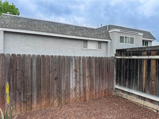 view of home's exterior featuring fence, stucco siding, mansard roof, and roof with shingles