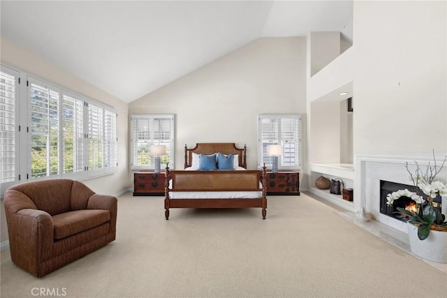 carpeted bedroom featuring high vaulted ceiling and a lit fireplace