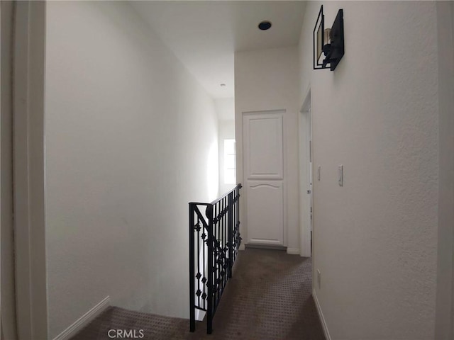 corridor with an upstairs landing, dark carpet, and baseboards