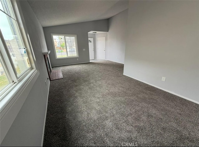 carpeted empty room with baseboards, arched walkways, and vaulted ceiling