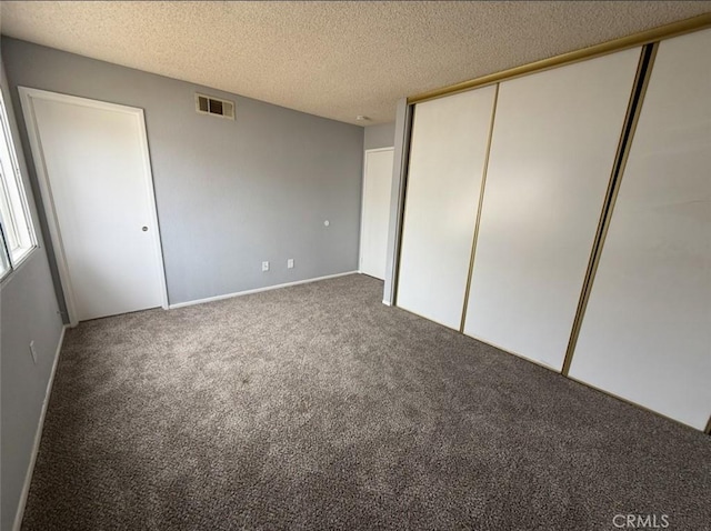 unfurnished bedroom with a textured ceiling, visible vents, carpet, and a closet