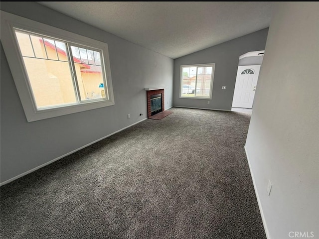 unfurnished living room featuring a textured ceiling, a brick fireplace, baseboards, lofted ceiling, and carpet