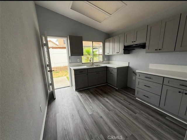 kitchen featuring under cabinet range hood, a sink, gray cabinets, and lofted ceiling