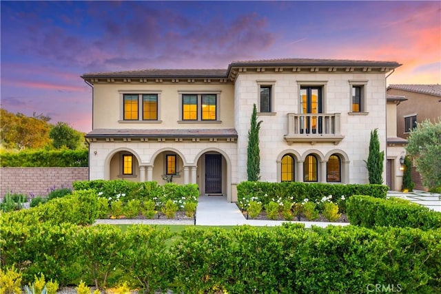 mediterranean / spanish-style home featuring a porch, a balcony, stone siding, and stucco siding