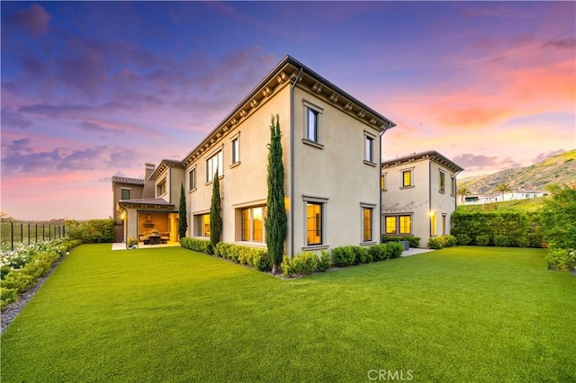 rear view of property featuring a lawn, fence, and stucco siding