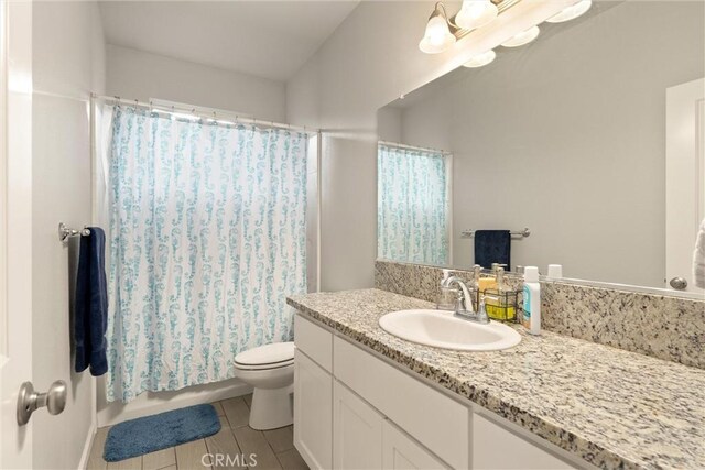bathroom featuring toilet, tile patterned flooring, shower / bath combo with shower curtain, and vanity