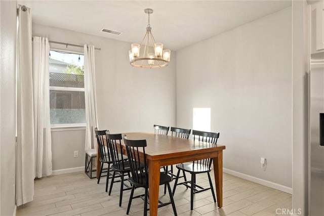 dining area featuring light wood finished floors, visible vents, a chandelier, and baseboards