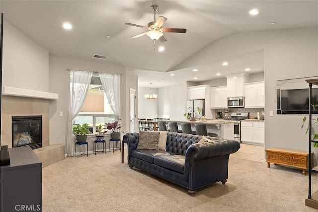 living area with lofted ceiling, light colored carpet, a tile fireplace, recessed lighting, and ceiling fan with notable chandelier