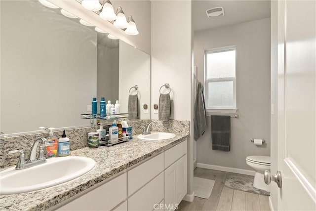 bathroom featuring double vanity, visible vents, toilet, and a sink