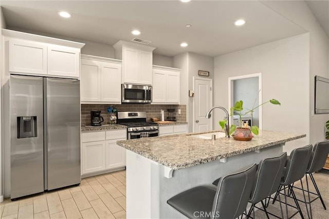 kitchen featuring a kitchen island with sink, decorative backsplash, stainless steel appliances, a sink, and white cabinetry