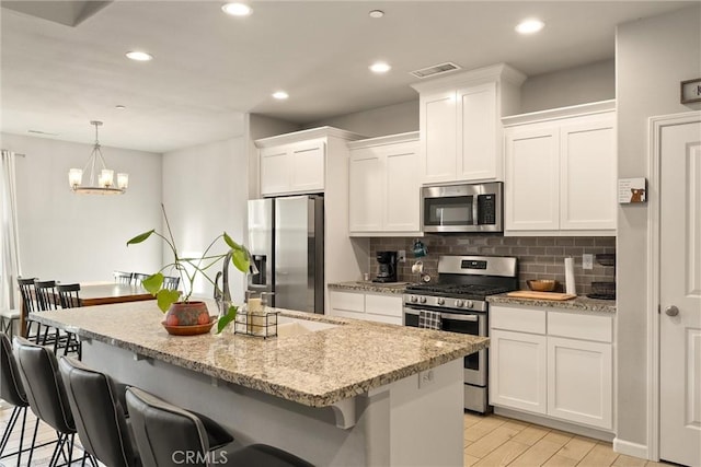 kitchen featuring a breakfast bar, visible vents, white cabinets, and stainless steel appliances