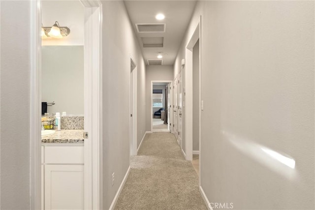 hall featuring baseboards, visible vents, and light carpet