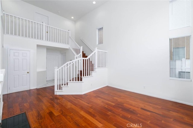 unfurnished living room with recessed lighting, a high ceiling, stairway, baseboards, and wood finished floors