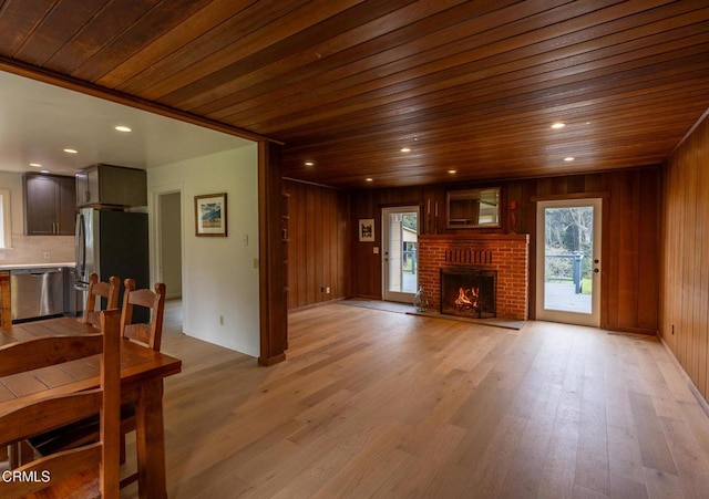 unfurnished living room featuring light wood-type flooring, wood walls, a wealth of natural light, and wood ceiling