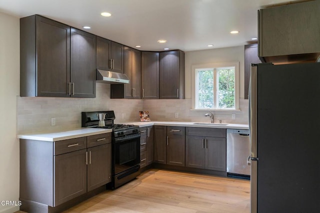 kitchen with tasteful backsplash, under cabinet range hood, appliances with stainless steel finishes, light wood finished floors, and a sink