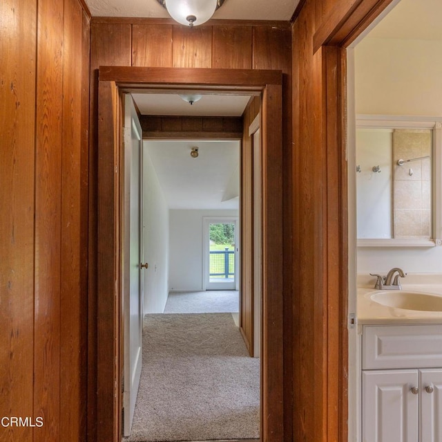 corridor featuring a sink, wood walls, and carpet