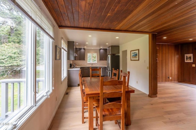 dining room featuring wooden walls, baseboards, light wood-style flooring, and wood ceiling