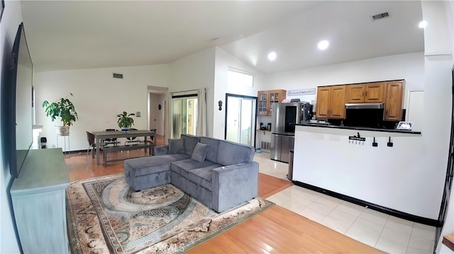 living room with light wood-type flooring, visible vents, and high vaulted ceiling