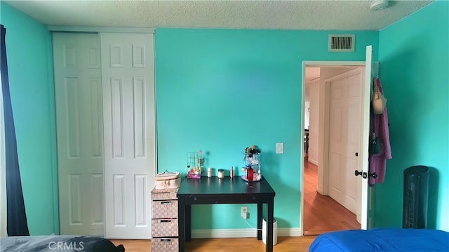 bedroom with a textured ceiling, a closet, visible vents, and wood finished floors