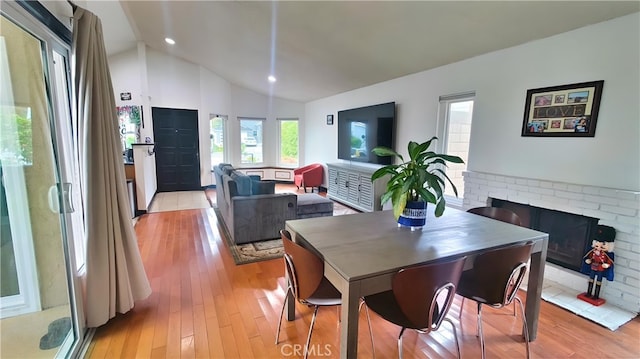 dining room featuring high vaulted ceiling, light wood-style flooring, a brick fireplace, and recessed lighting