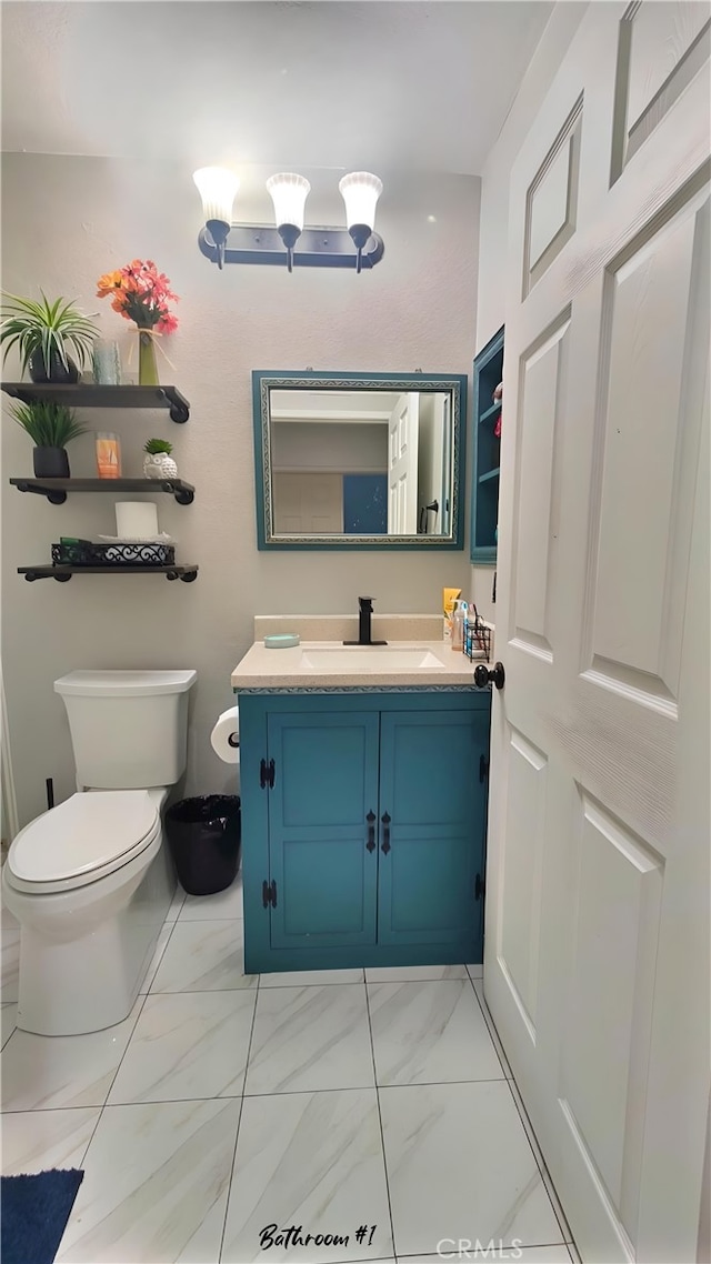 half bathroom featuring toilet, marble finish floor, and vanity