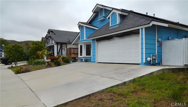 view of front of house featuring driveway, roof with shingles, a garage, and fence
