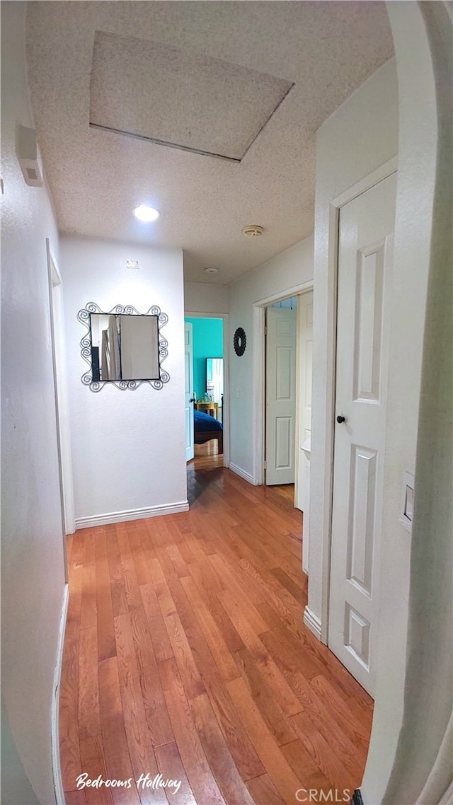 hallway with light wood finished floors, a textured ceiling, baseboards, and recessed lighting