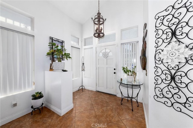 tiled entrance foyer featuring baseboards, high vaulted ceiling, and a notable chandelier