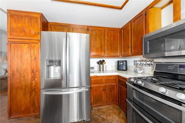 kitchen featuring appliances with stainless steel finishes, tile counters, brown cabinets, and tile patterned floors