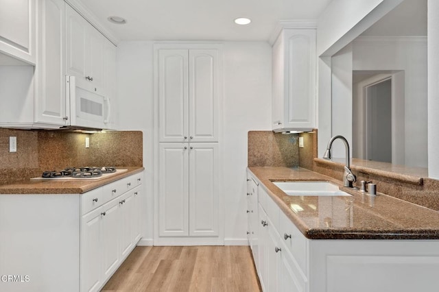 kitchen with white appliances, dark stone counters, light wood-style floors, white cabinets, and a sink