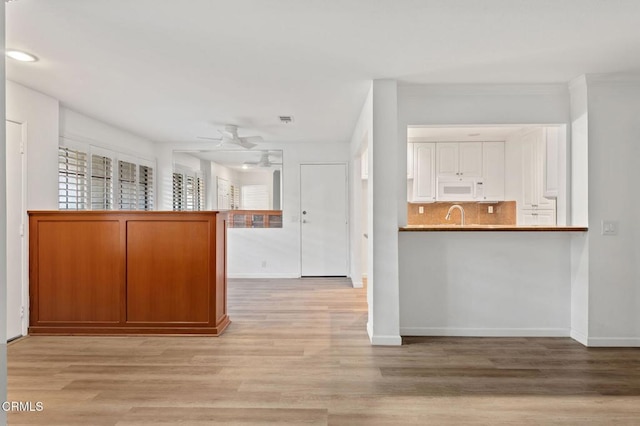 kitchen featuring ceiling fan, tasteful backsplash, light wood-type flooring, white microwave, and baseboards