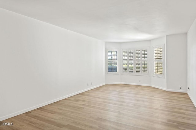 spare room with baseboards and light wood-style floors