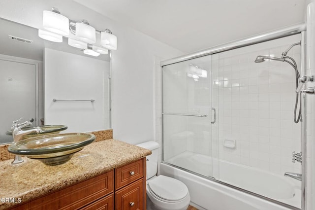 bathroom with visible vents, bath / shower combo with glass door, toilet, and vanity