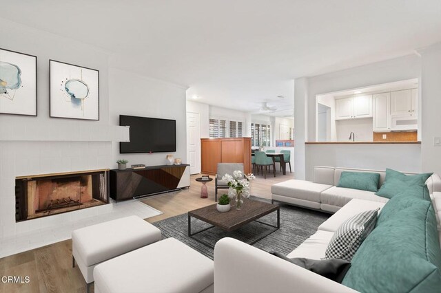 living room featuring wood finished floors, ceiling fan, and a brick fireplace