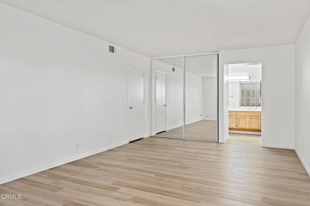 unfurnished bedroom with visible vents, light wood-type flooring, ensuite bath, and baseboards