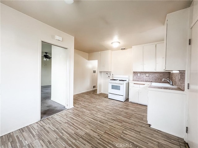 kitchen with decorative backsplash, gas range gas stove, a sink, light countertops, and white cabinetry